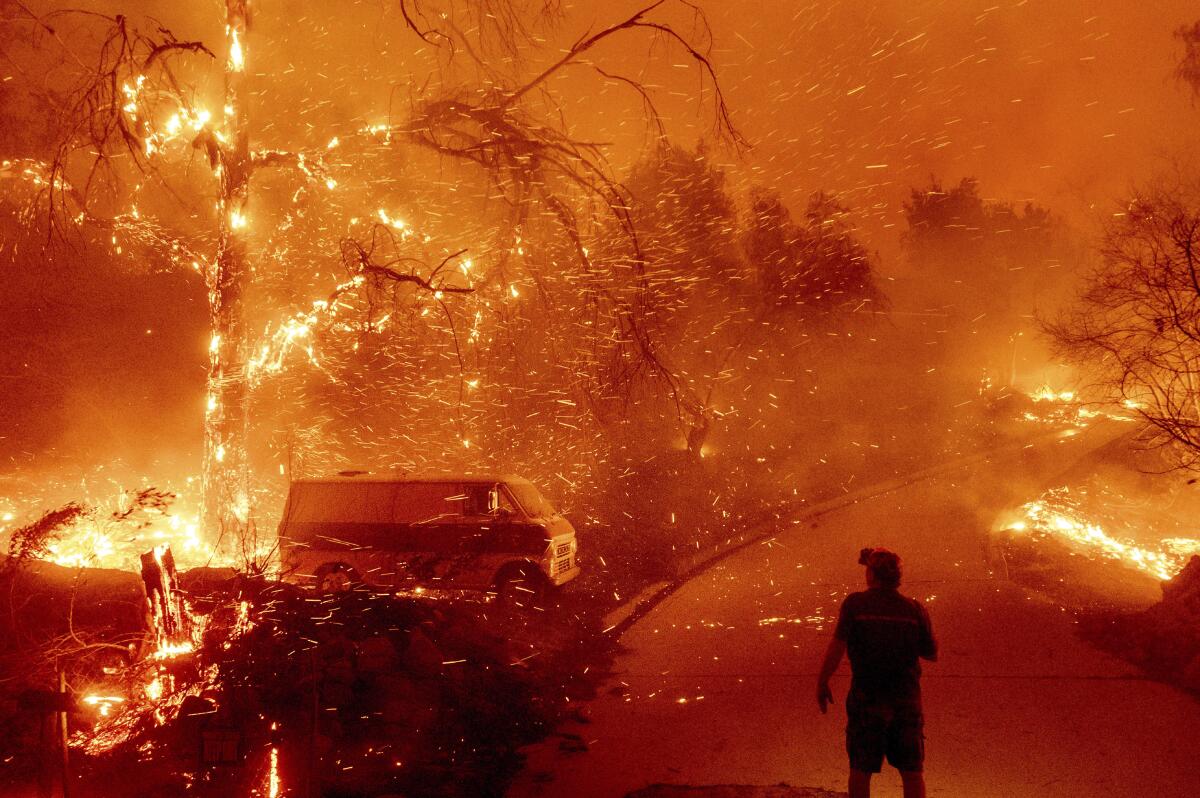 ARCHIVO - Bruce McDougal mira las brasas volar sobre su propiedad durante el incendio Bond 