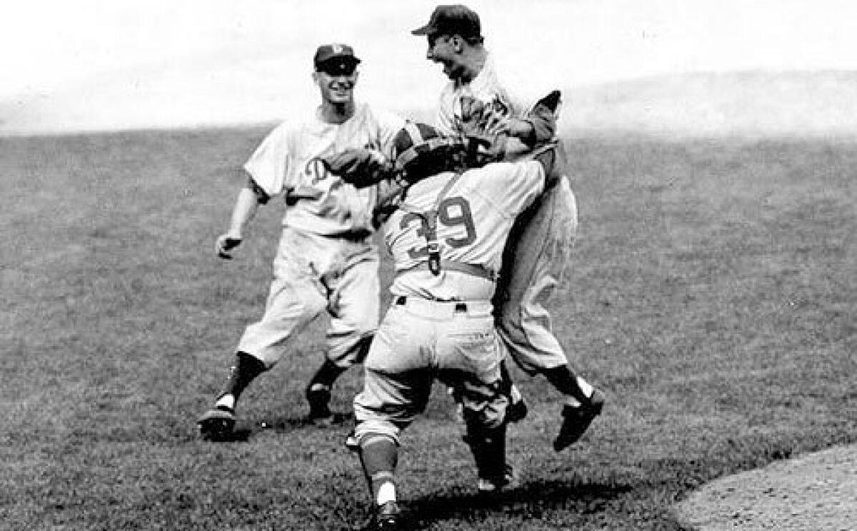 Brooklyn Dodgers pitcher Johnny Podres is lifted by catcher Roy Campanella as third baseman Don Hoak joins in.