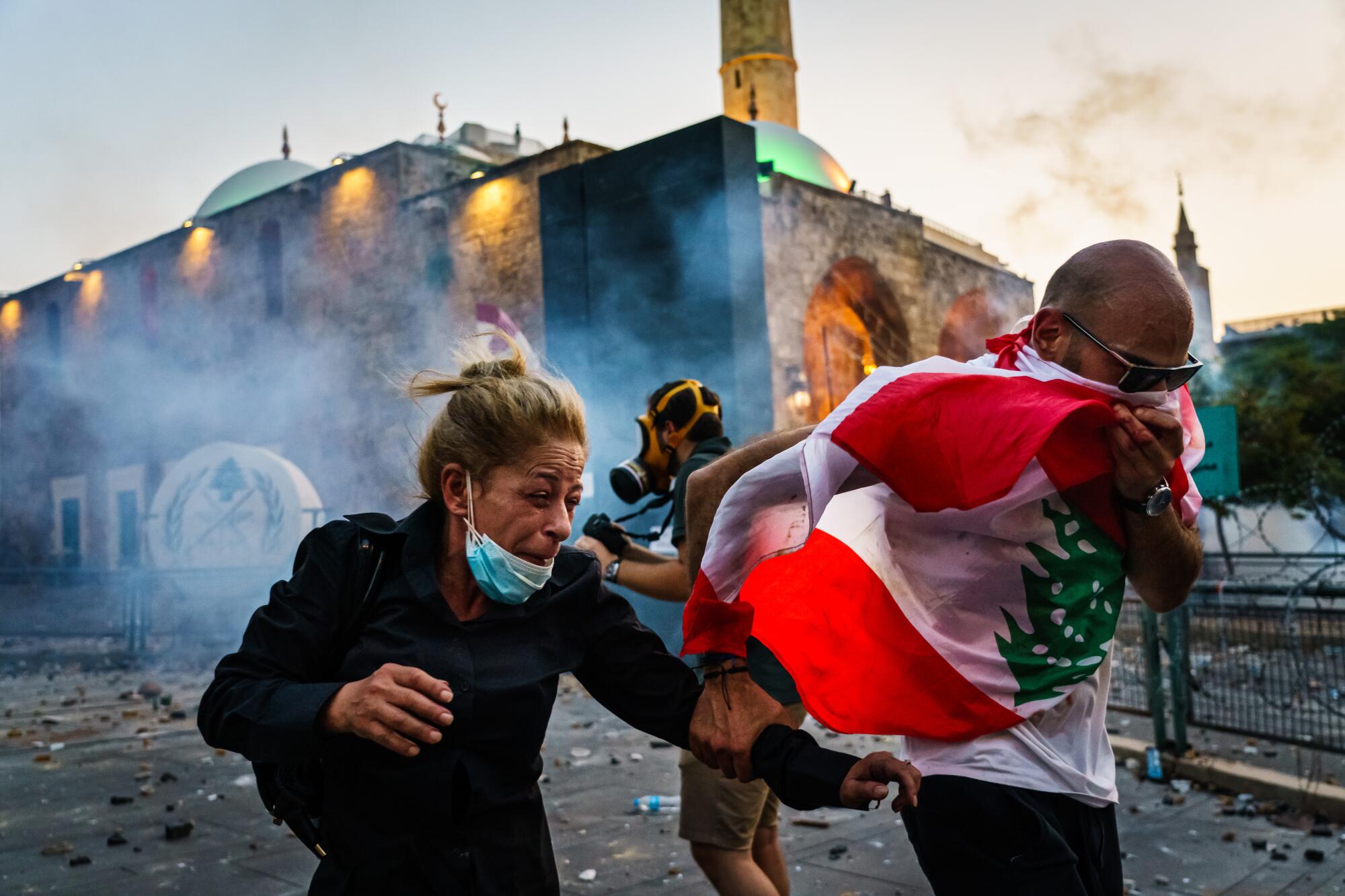 A woman grimaces and a man covers his nose and mouth with a flag as they run.