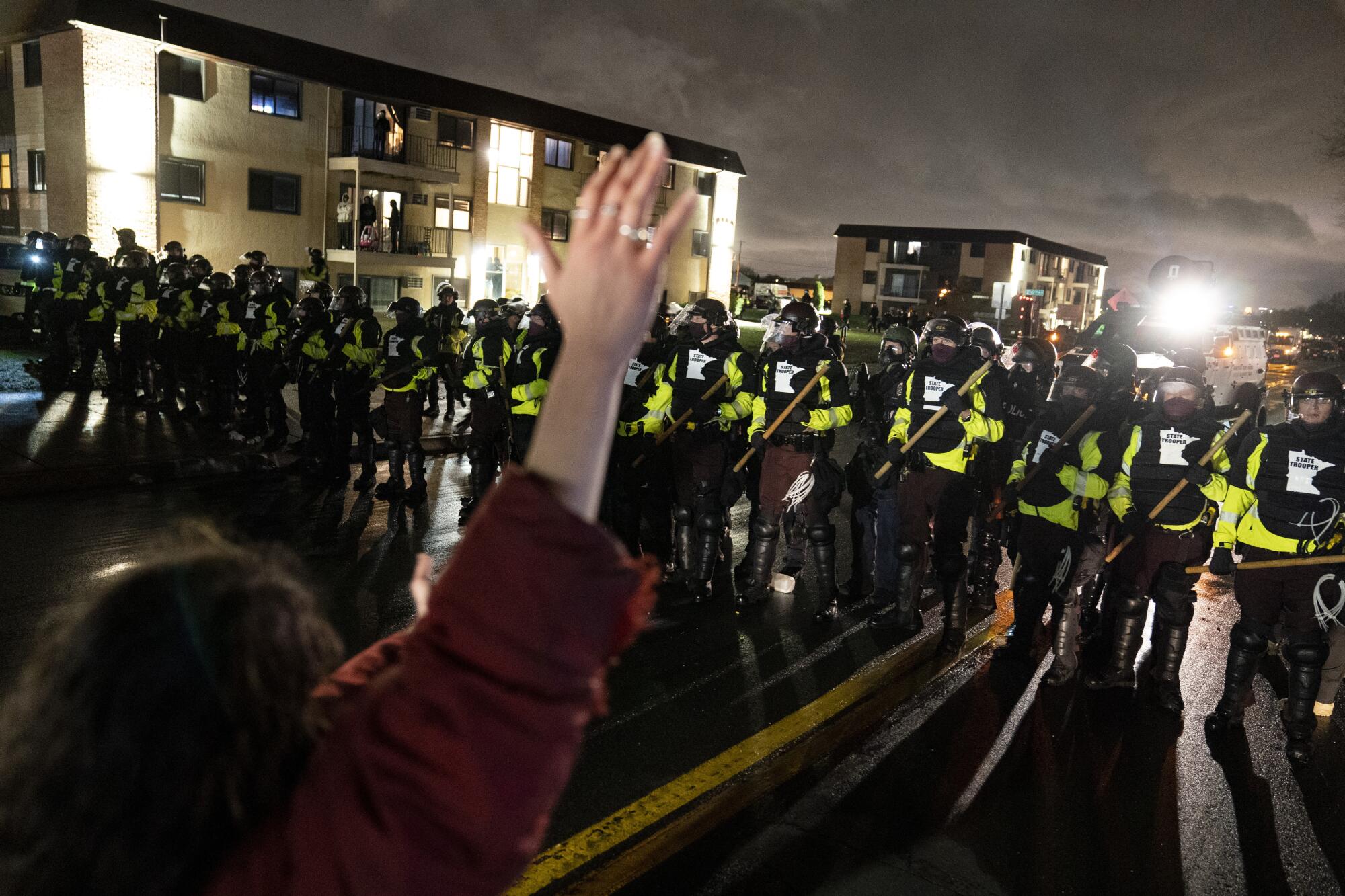 A person raises their hand facing a line of police