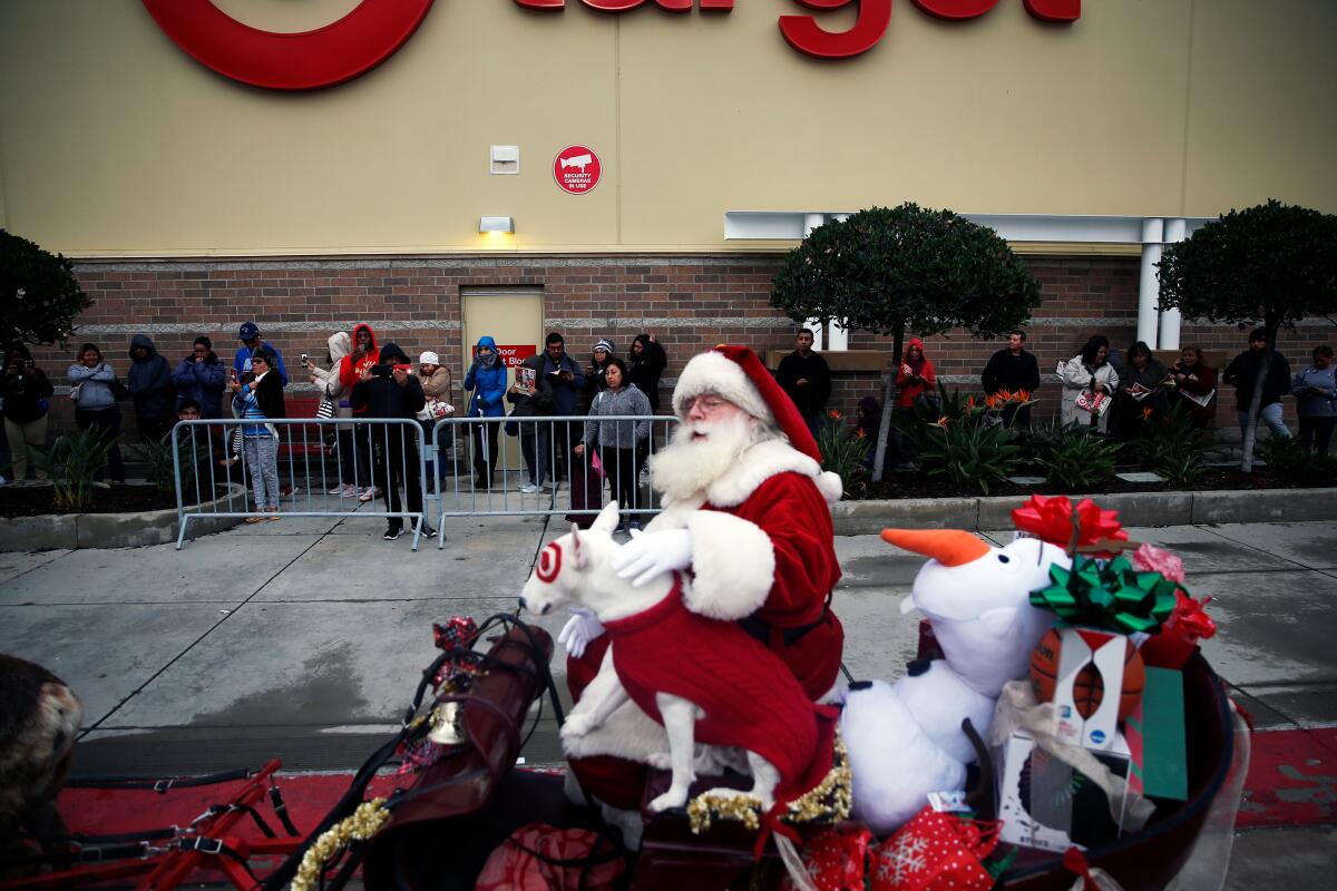 Santa and the Target store mascot, Bullseye the dog, in a sled with a line of people in the background.