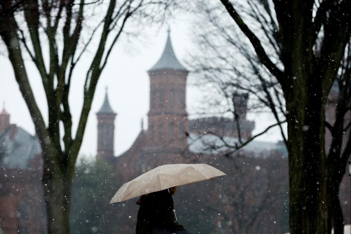 The Smithsonian Institution Building known as the Castle is visible as a pedestrian walks through light snow on the first day of spring in Washington.