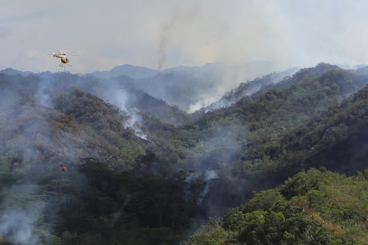 Army helicopter carrying water to douse a wildfire burning in a remote mountainous area.
