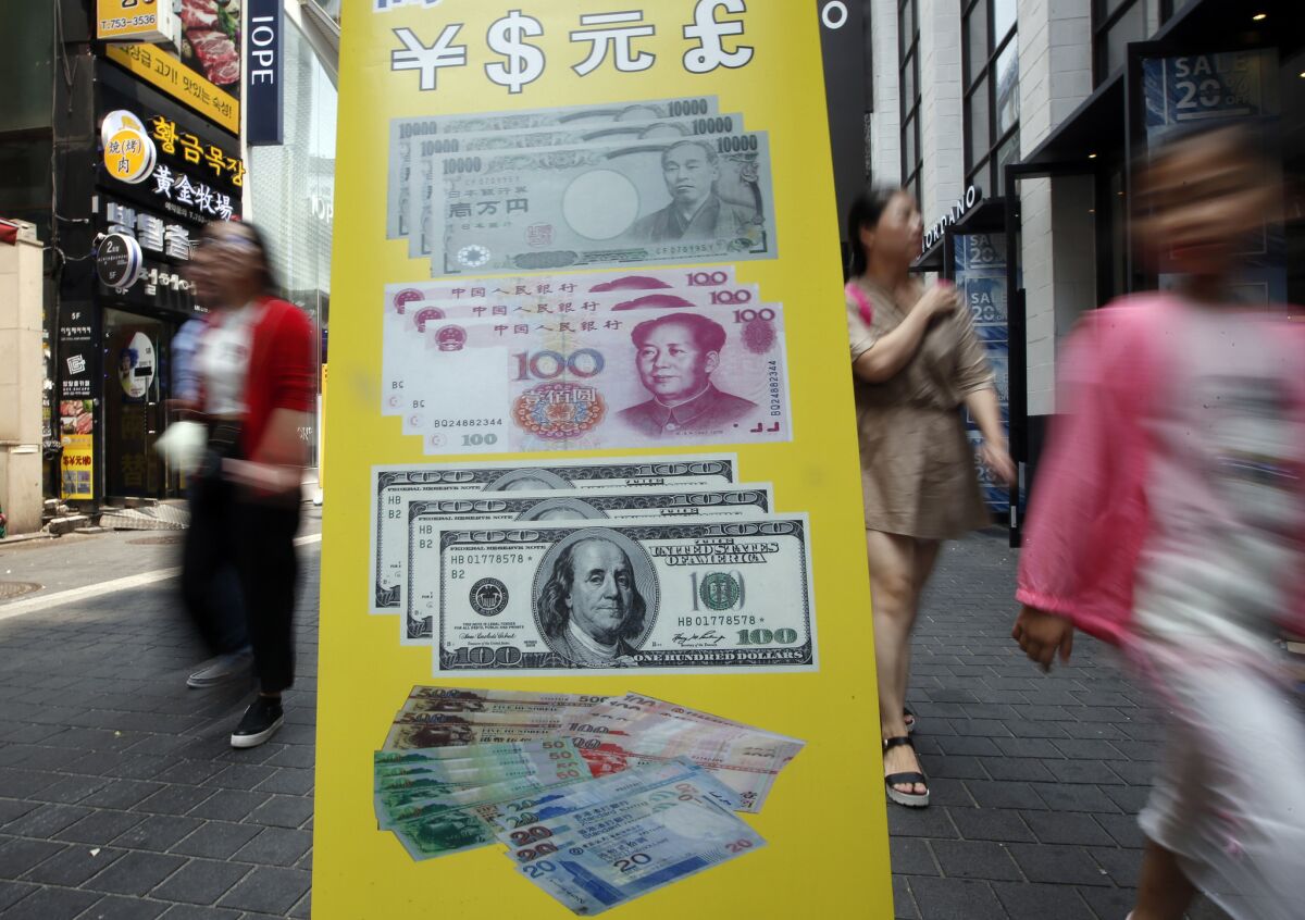 Visitors walk by signs displaying currency exchange rates at downtown Seoul, South Korea.
