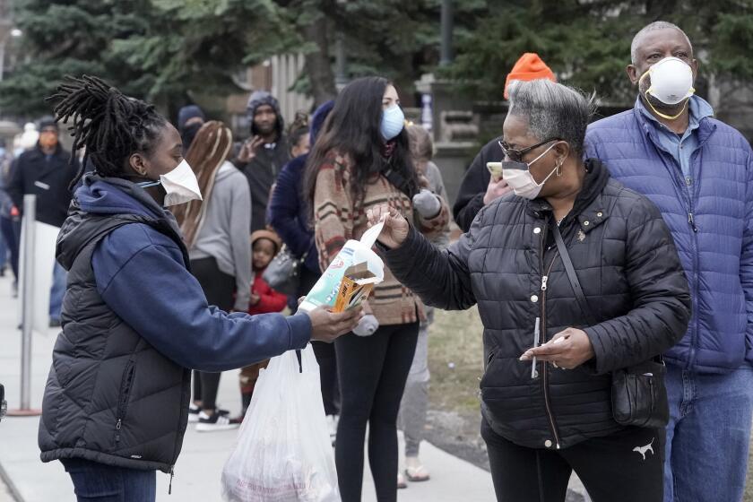 FILE - In this April 7, 2020, file photo, a worker hands out disinfectant wipes and pens as voters line up outside Riverside High School for Wisconsin's primary election in Milwaukee. Many Black voters are skeptical of voting by mail even as states seek to expand that option during the coronavirus pandemic. Decades of racism and voter disenfranchisement are at the heart of the uneasy choice facing Black voters. (AP Photo/Morry Gash, File)