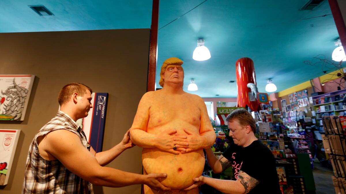 Robert Crichton, left, and Matt Kennedy move a statue depicting a nude Donald Trump back outside to the entrance of Soap Plant Wacko in Los Feliz.