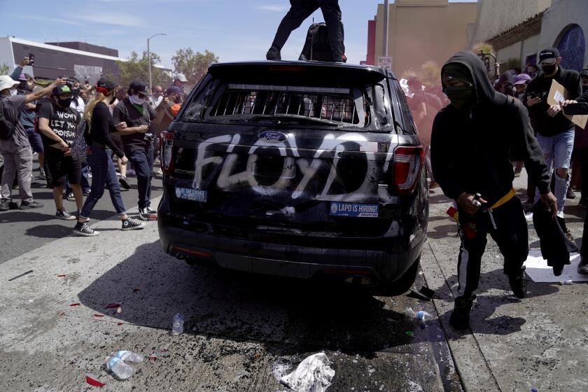 LOS ANGELES, CA - MAY 30: A police car is spray-painted with the name Floyd during a demonstration at Pan Pacific Park on Saturday, May 30, 2020 in Los Angeles, CA. Protests erupted across the country, with people outraged over the death of George Floyd, a black man killed after a white Minneapolis police officer pinned him to the ground with his knee. (Kent Nishimura / Los Angeles Times)
