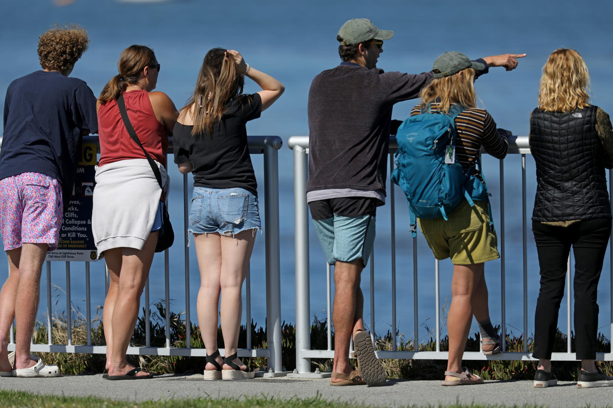 People stand along a fence overlooking the ocean
