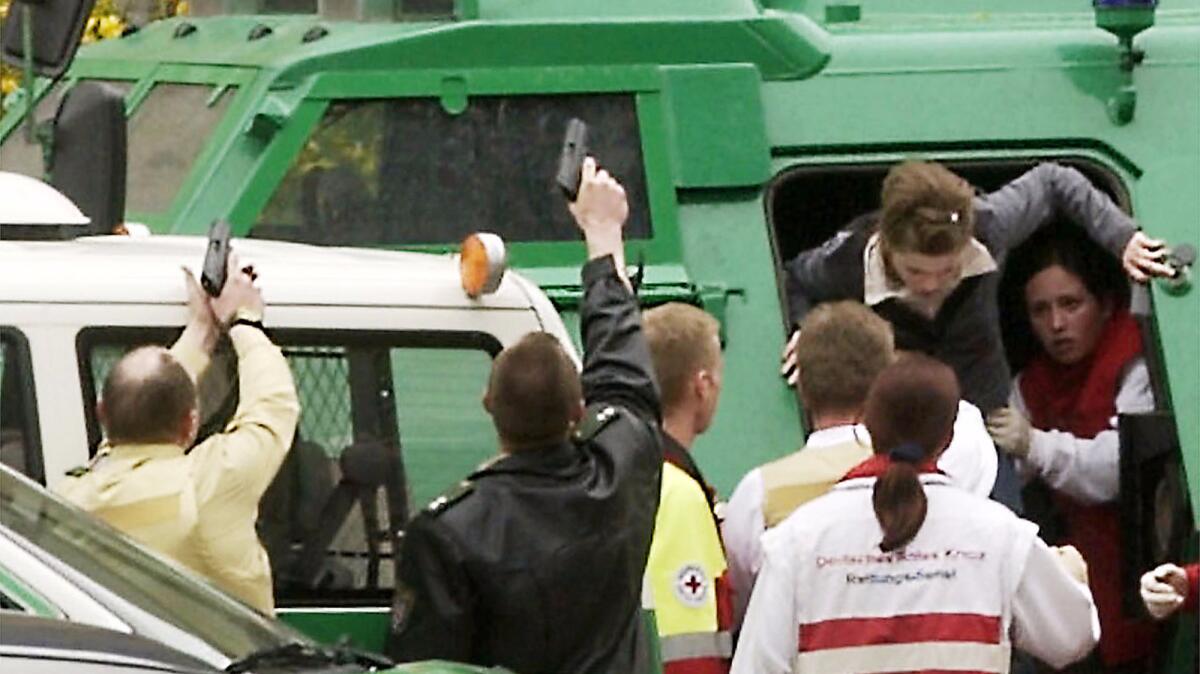 A girl is helped by rescue workers out of a police armored vehicle as officers aim their guns during a school shooting in Erfurt, Germany, in 2002.