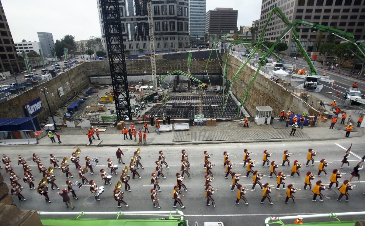 A marching band passes a giant pit at a construction site.