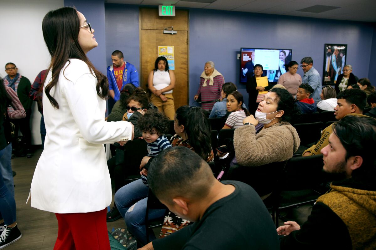 A woman stands and talks in front of a room full of people.