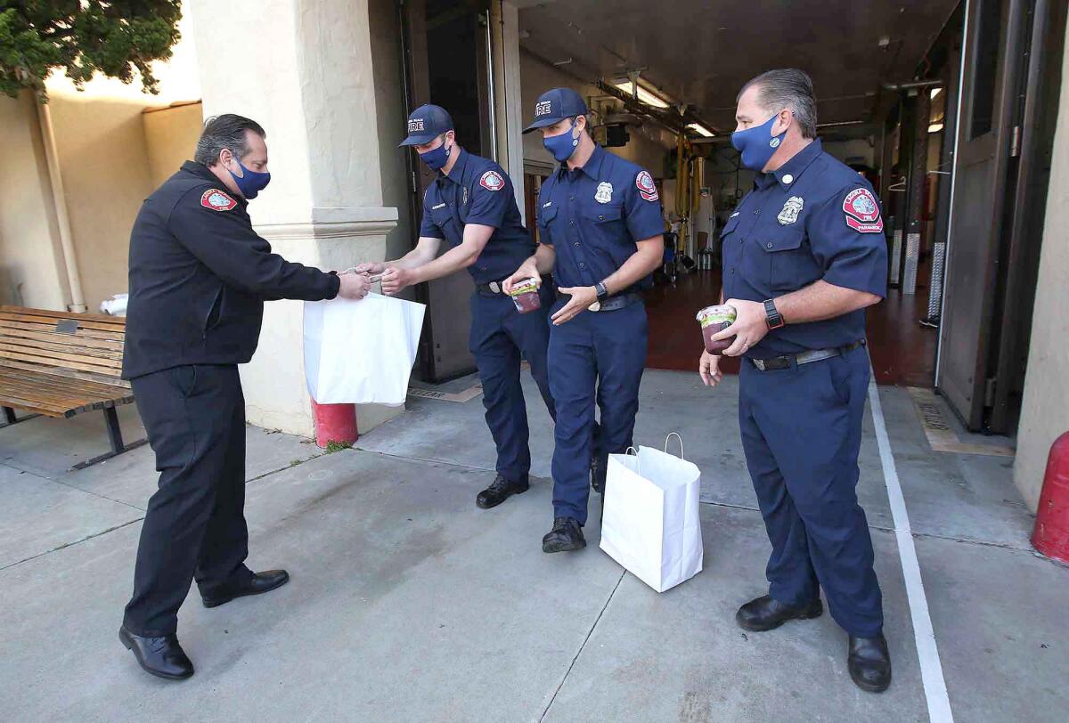 Laguna Beach Fire Chief Michael Garcia, left, hands prepared acai and breakfast bowls to firefighters Brandon Hawkins, Pat Cary and Capt. Eric Lether on Monday.