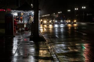 SANTA ANA, CA - DECEMBER 27, 2022: On a rain slicked evening, a street vendor sells his food on the sidewalk off McFadden Avenue on December 27, 2022 in Santa Ana, California.The City of Santa Ana is cracking down on unlicensed street vendors in the city. In the past two months, the city has shut down 100 of the businesses temporarily. The businesses were back up within a few days moving to different locations. (Gina Ferazzi / Los Angeles Times)