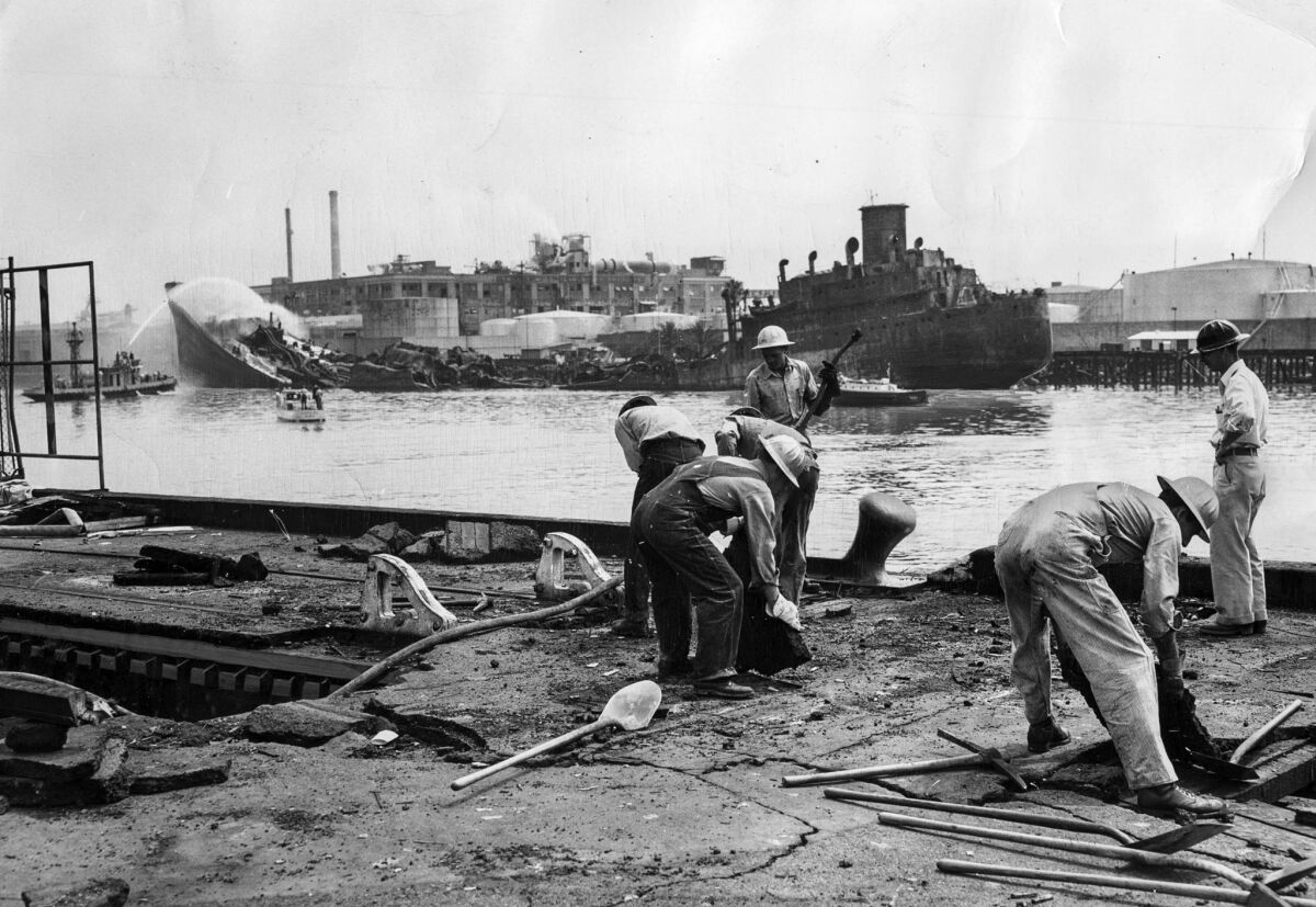 June 23, 1947: The day after an explosion destroyed the tanker Markay, background, workers tear up asphalt to get at flames underneath pier.