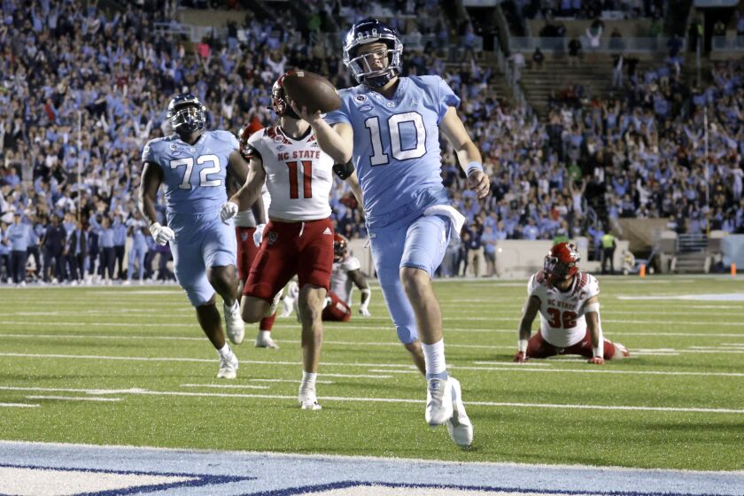 North Carolina quarterback Drake Maye (10) rolls into the end zone for a touchdown as North Carolina State linebackers Payton Wilson (11) and Drake Thomas (32) trail during the second half of an NCAA college football game Friday, Nov. 25, 2022, in Chapel Hill, N.C. (AP Photo/Chris Seward)