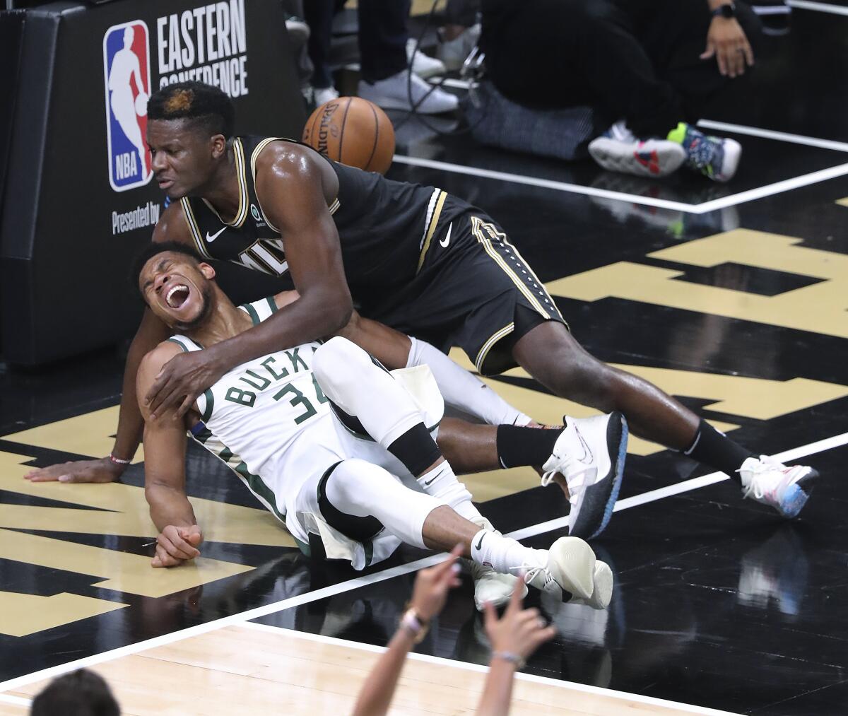 Atlanta Hawks center Clint Capela, top, and Milwaukee Bucks forward Giannis Antetokounmpo fall to the court.