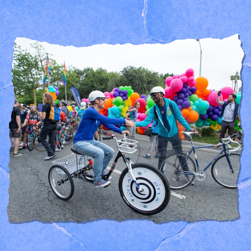 Two people on bikes shake hands. In the background are balloons and other cyclists.
