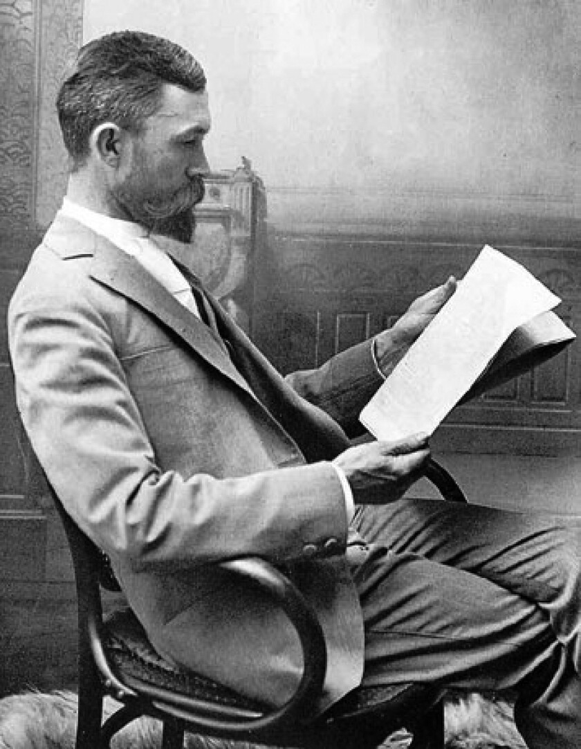A historic black-and-white photo of a man reading in a chair.