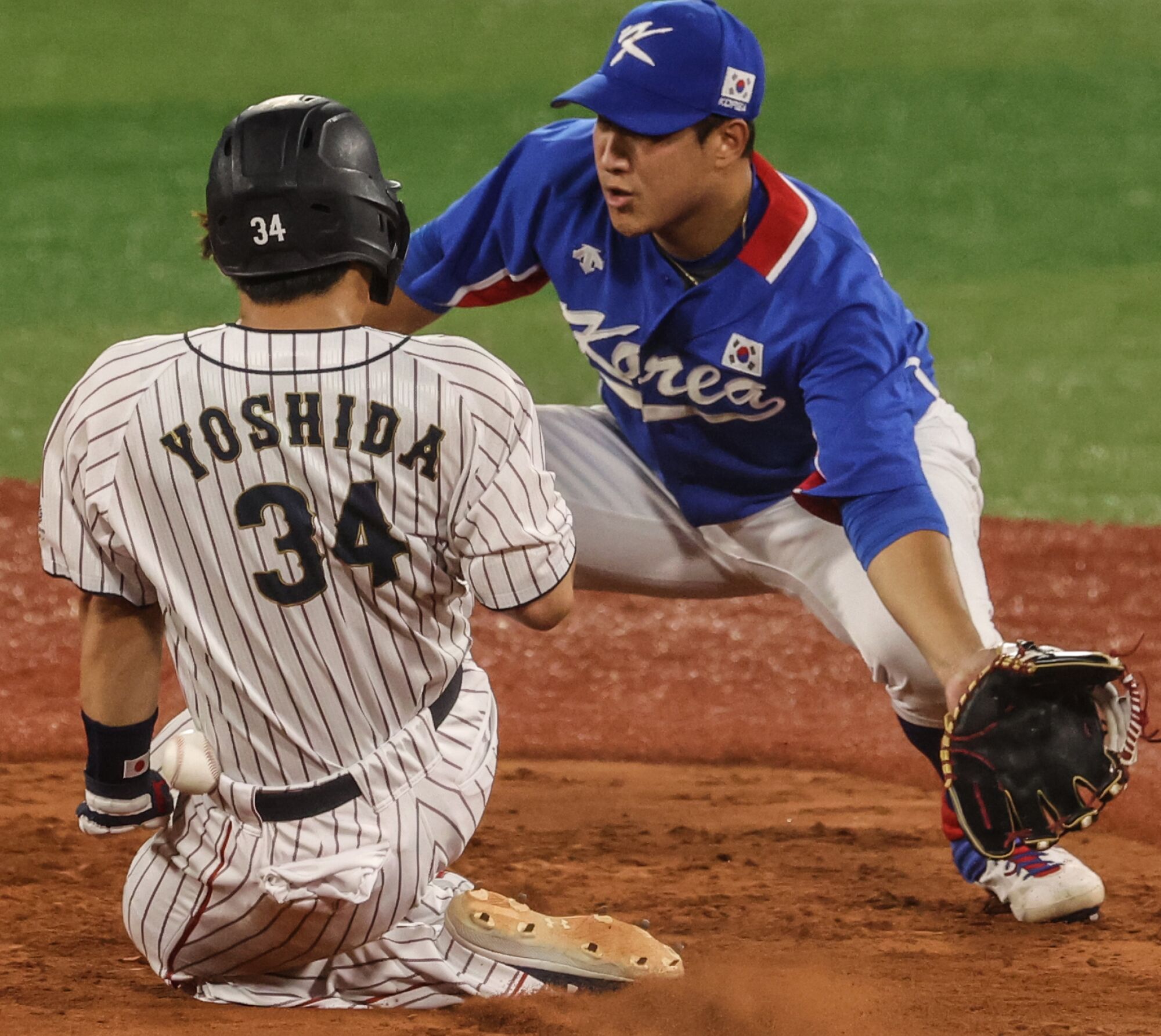 Japan's Masataka Yoshida is hit by the ball as he slides safely into second base in front of South Korea's Jaegyun Hwang.