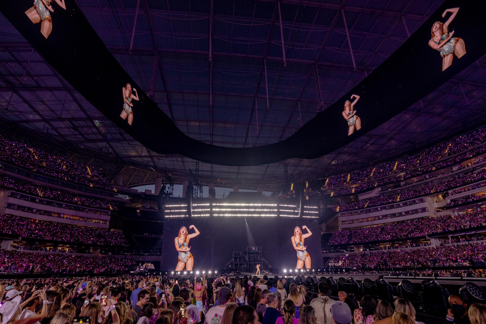 Taylor Swift performs while images of her are projected on big screens in a stadium.