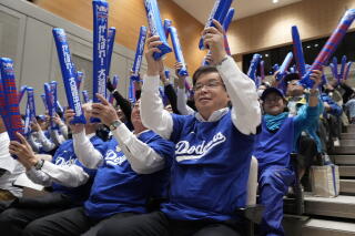 People in Dodger T-shirts hold up blue thundersticks in an auditorium.