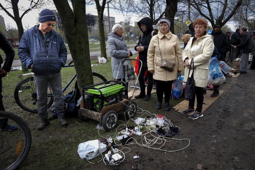 FILE - Local residents gather near a generator to charge their mobile devices in an area controlled by Russian-backed separatist forces in Mariupol, Ukraine, Friday, April 22, 2022. When Russian forces two months ago launched a military campaign against infrastructure in Ukraine, it opened an urgent second front far from the contact line: Along power lines, water mains, and heating systems, and in places like homes, schools, offices and churches. (AP Photo/Alexei Alexandrov, File)