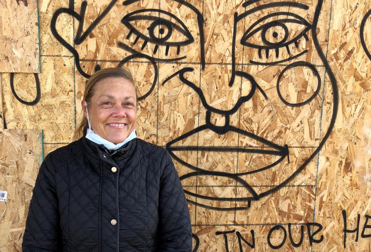 Linda Minshall stands in front of a mural on particleboard.