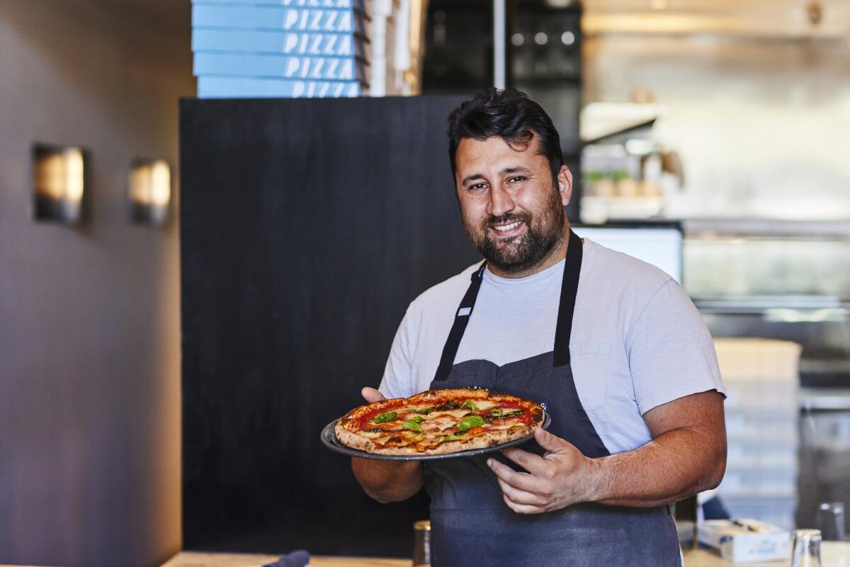 Pizzana chef Daniele Uditi holds a basil-topped pizza inside his restaurant.