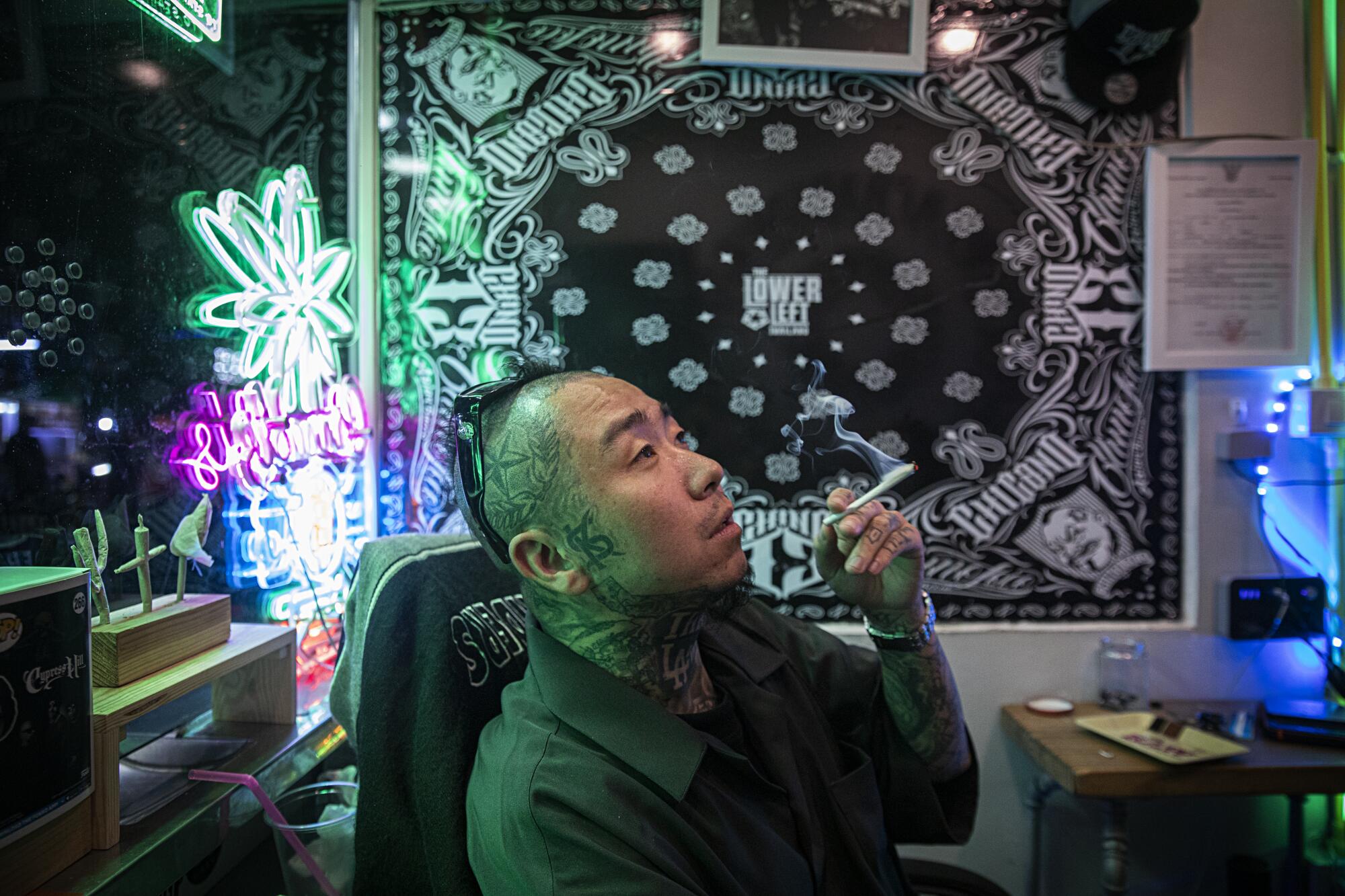 A man smokes a joint in a dark room with some neon lights.