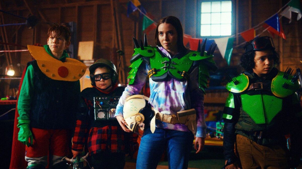 Four children with colorful armor and helmets are standing in a living room