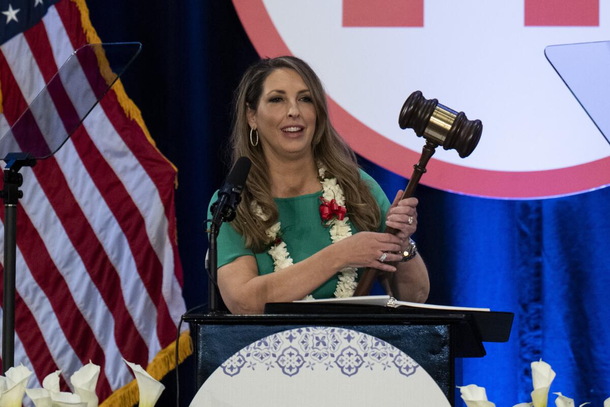 A woman at a podium holds a giant gavel.