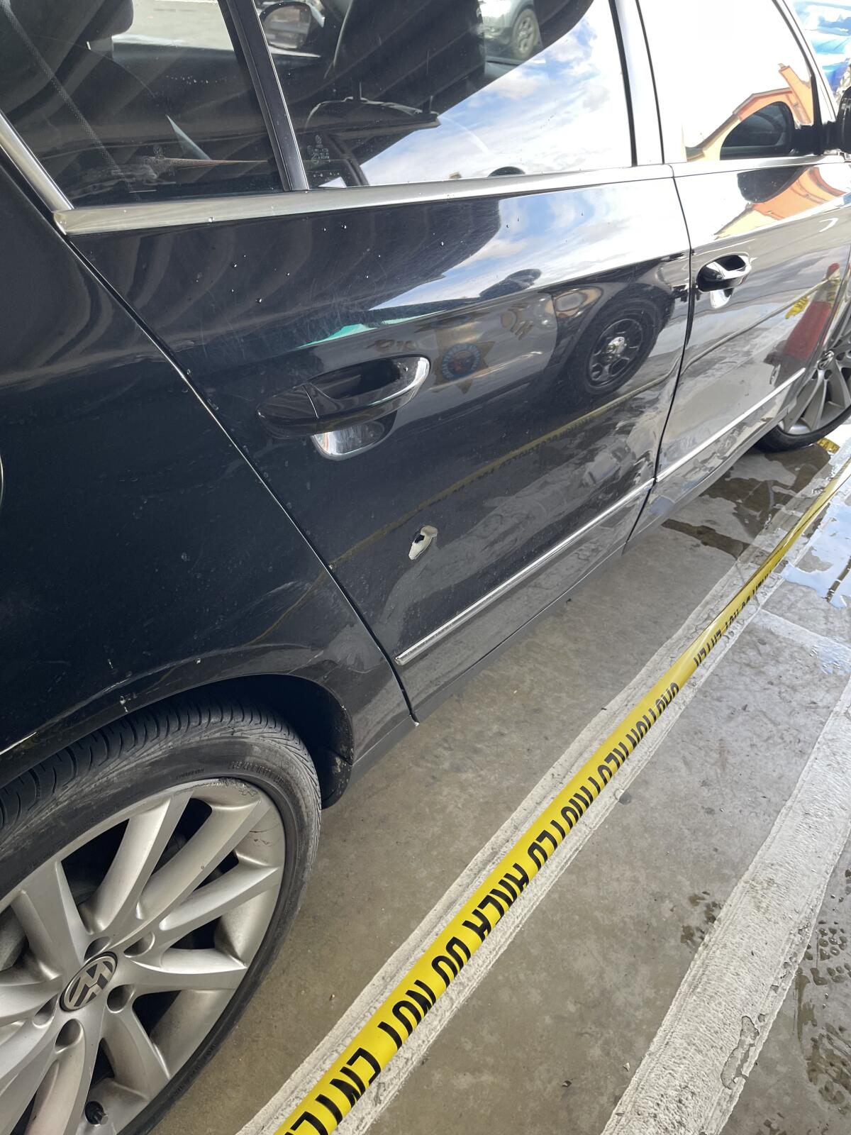 Caution tape marks off a car with a bullet hold in its rear passenger door.