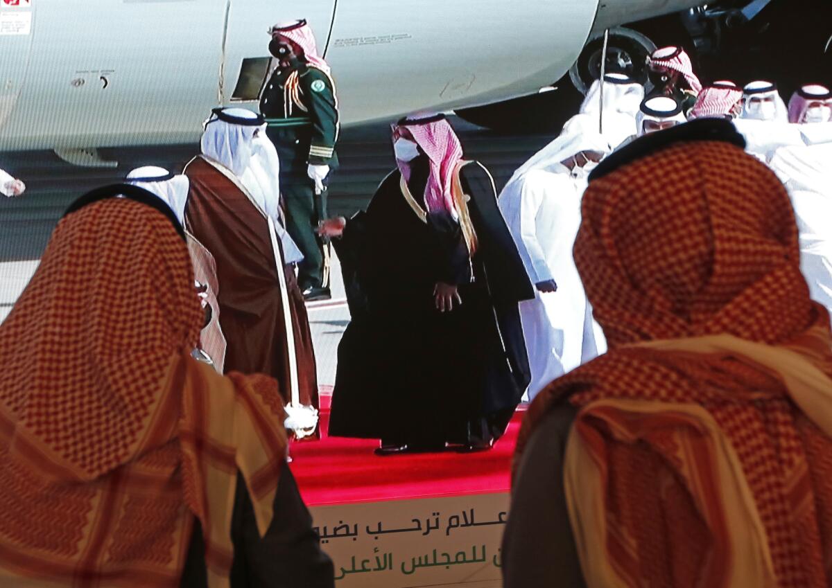 On an airport tarmac amid a crowd, Saudi's crown prince extends his hand in greeting to Qatar's monarch.