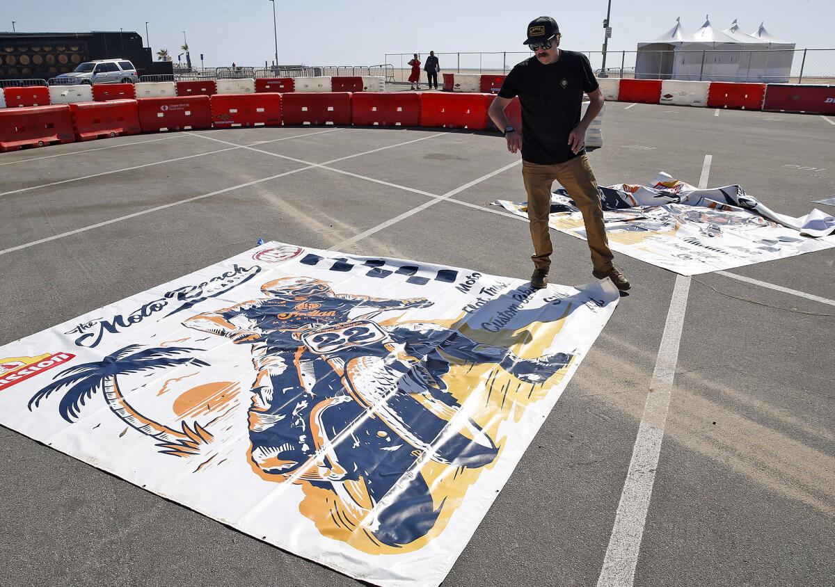 Cameron Brewer lays out event banners for the Moto Beach Classic happening at Bolsa Chica State Beach on Saturday.