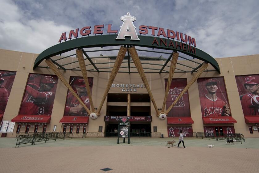 A woman walks her dog by an empty Angel Stadium of Anaheim in Anaheim, Calif., Wednesday, March 25, 2020. There will be empty ballparks on what was supposed to be Major League Baseball's opening day, with the start of the Major League Baseball regular season indefinitely on hold because of the coronavirus pandemic. (AP Photo/Chris Carlson)