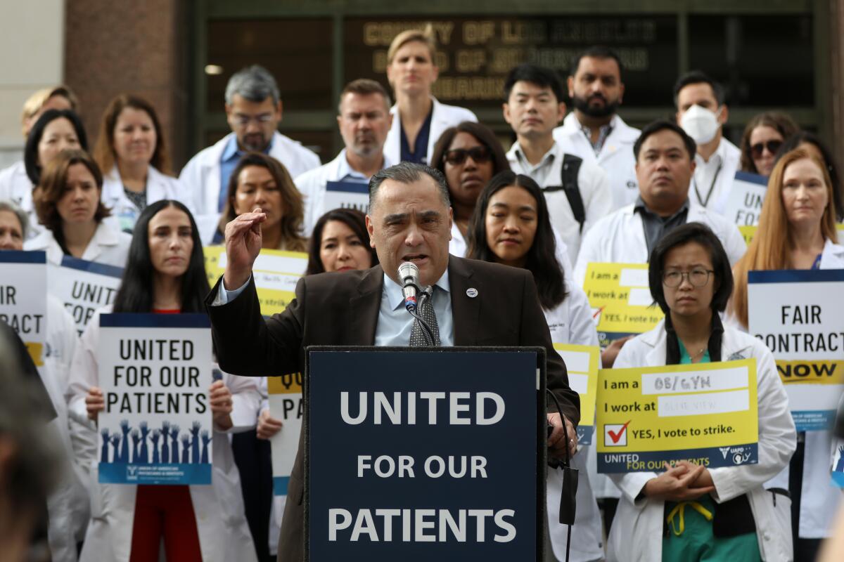 A man speaks a lectern as people in white medical coats stand behind him.