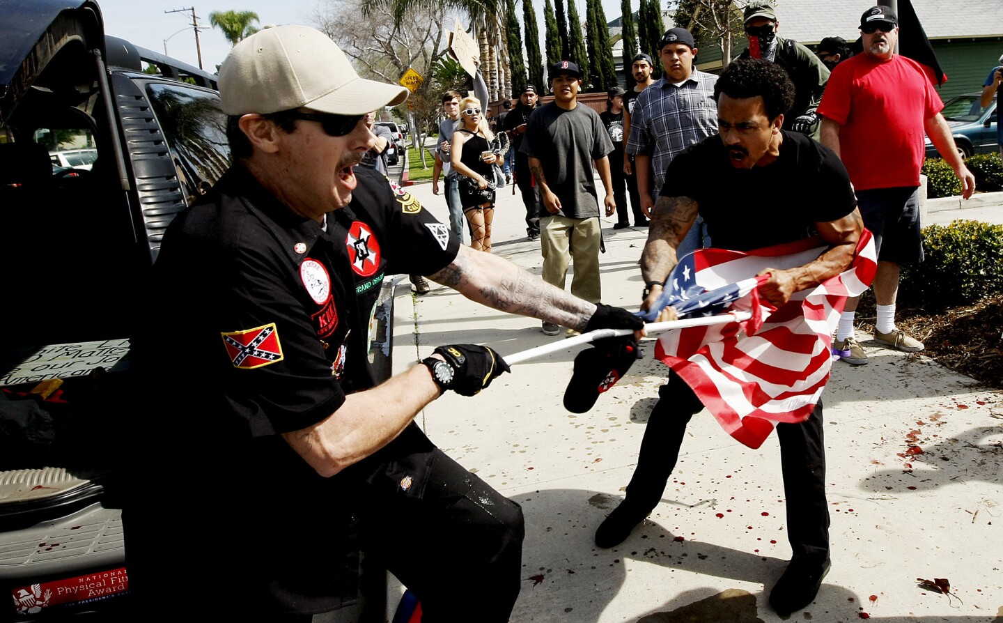A Ku Klux Klansman, left, struggles with a protester for an American flag after members of the KKK tried to start a "White Lives Matter" rally at Pearson Park in Anaheim on Saturday. Three people were treated at the scene for stab wounds, and 13 people were arrested.