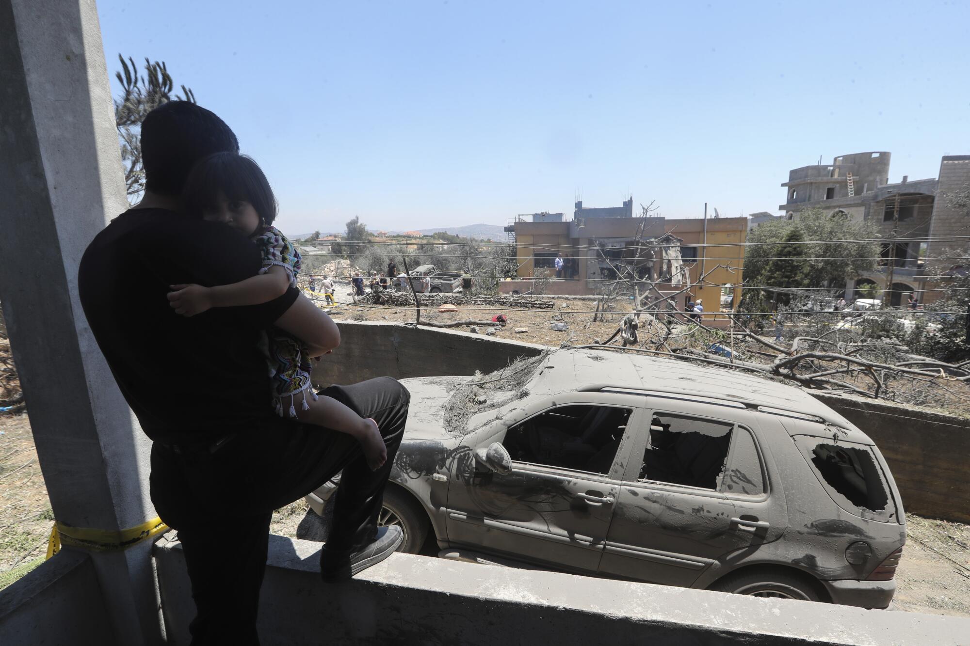 A man holds his child as he looks at the damage that was caused by an Israeli airstrike in the village of Jmaijmeh, Lebanon.