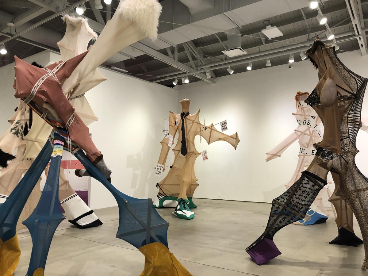 A room full of large-scale figure sculptures in stiff poses are made from fabric stretched over slender wood frames