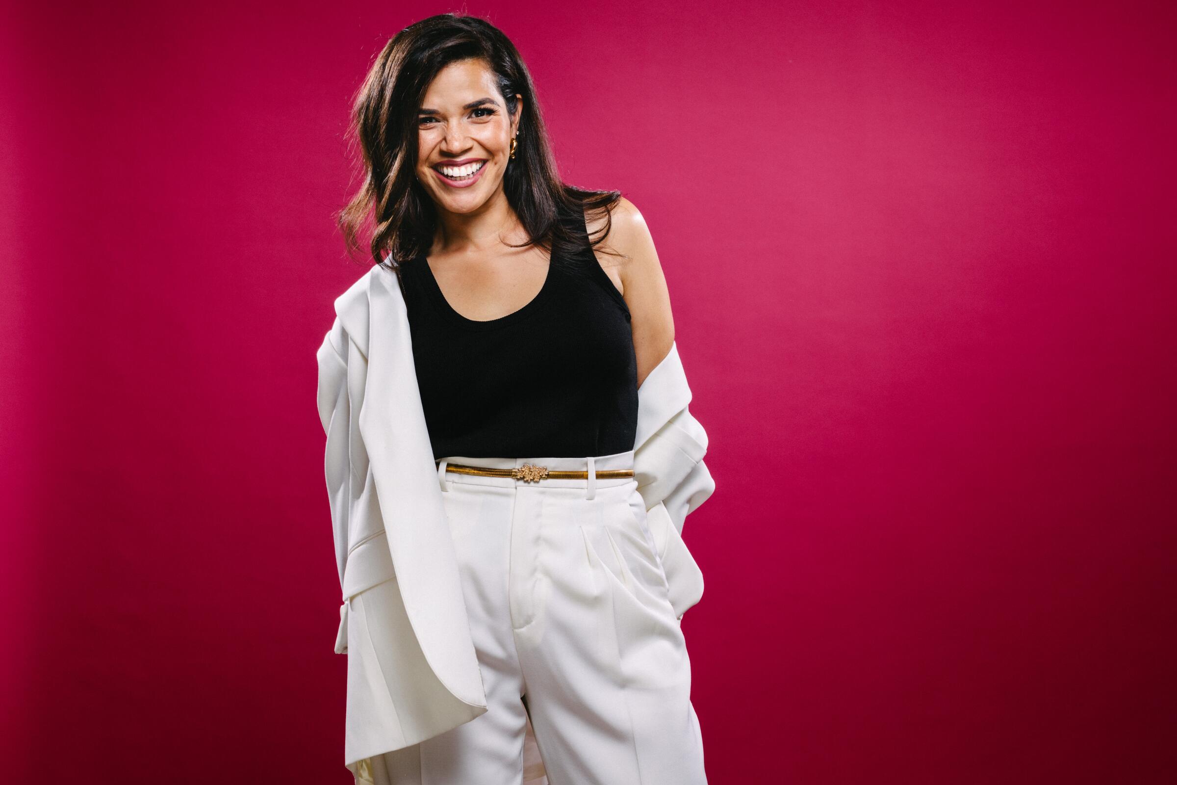 America Ferrera wears a pantsuit with the jacket pulled off one shoulder for a portrait.