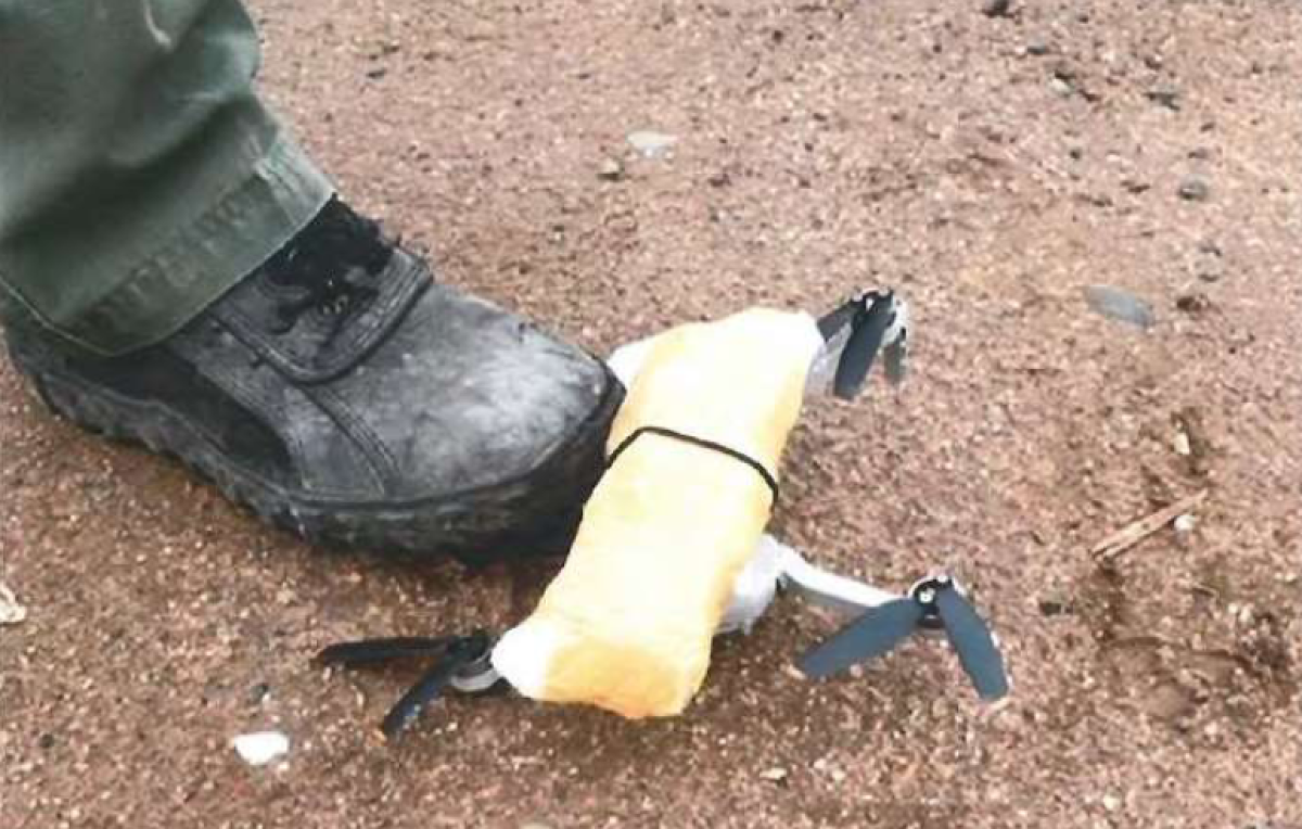 A small unmanned aircraft carrying 0.57 pounds of methamphetamine is held down by a Border Patrol agent's boot