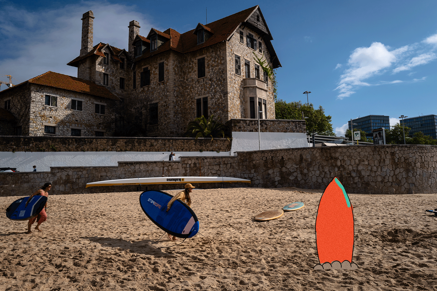 Two people walk on a beach with surfboards in Cascais, Portugal.