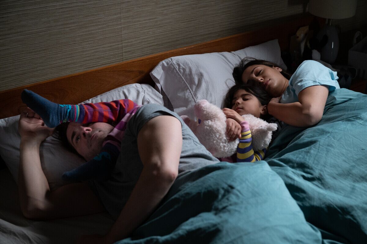 A child lays across the pillows of a bed with her feet on her dad's face.