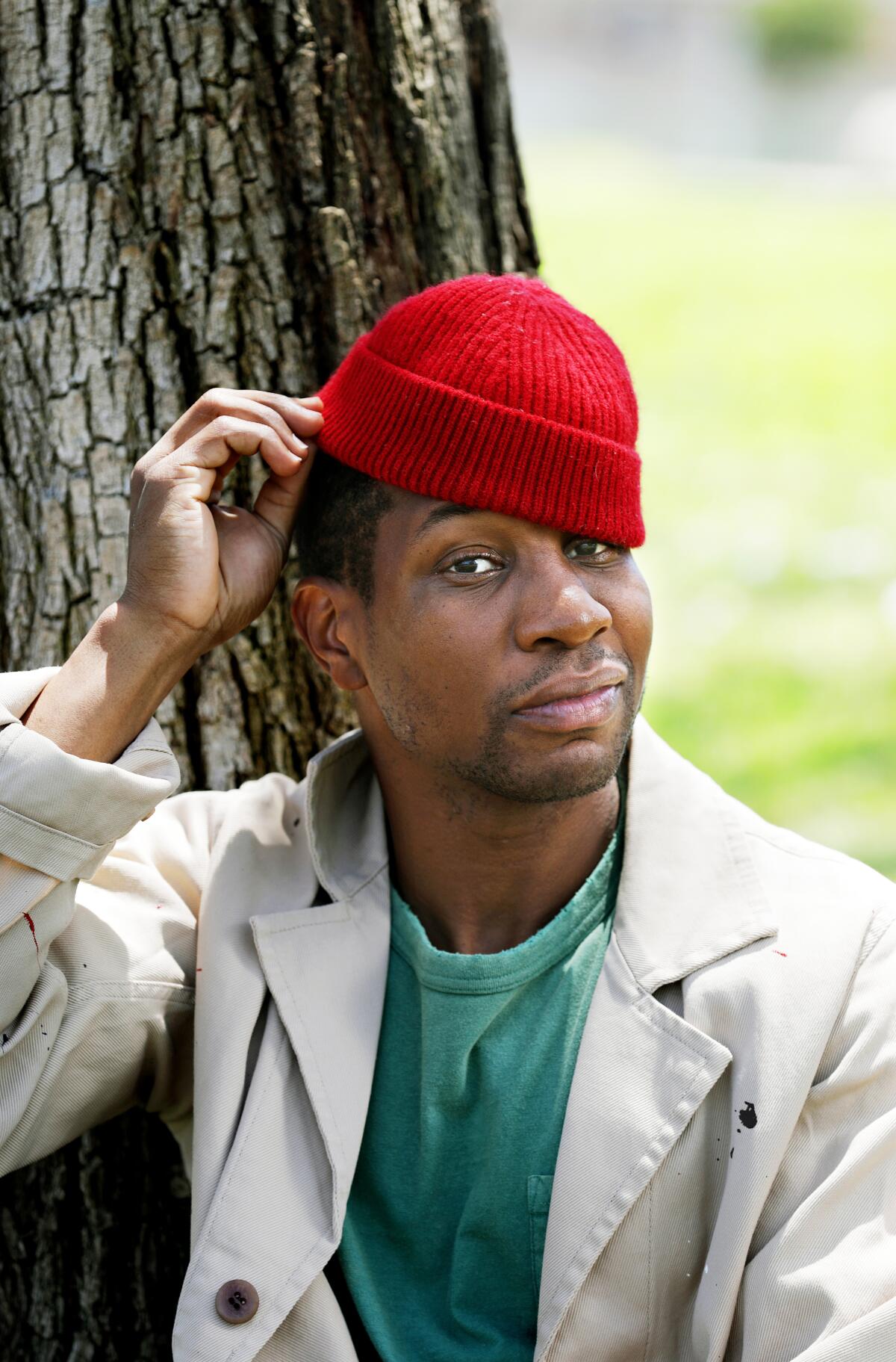  Jonathan Majors sits against a tree, touching his knit cap.