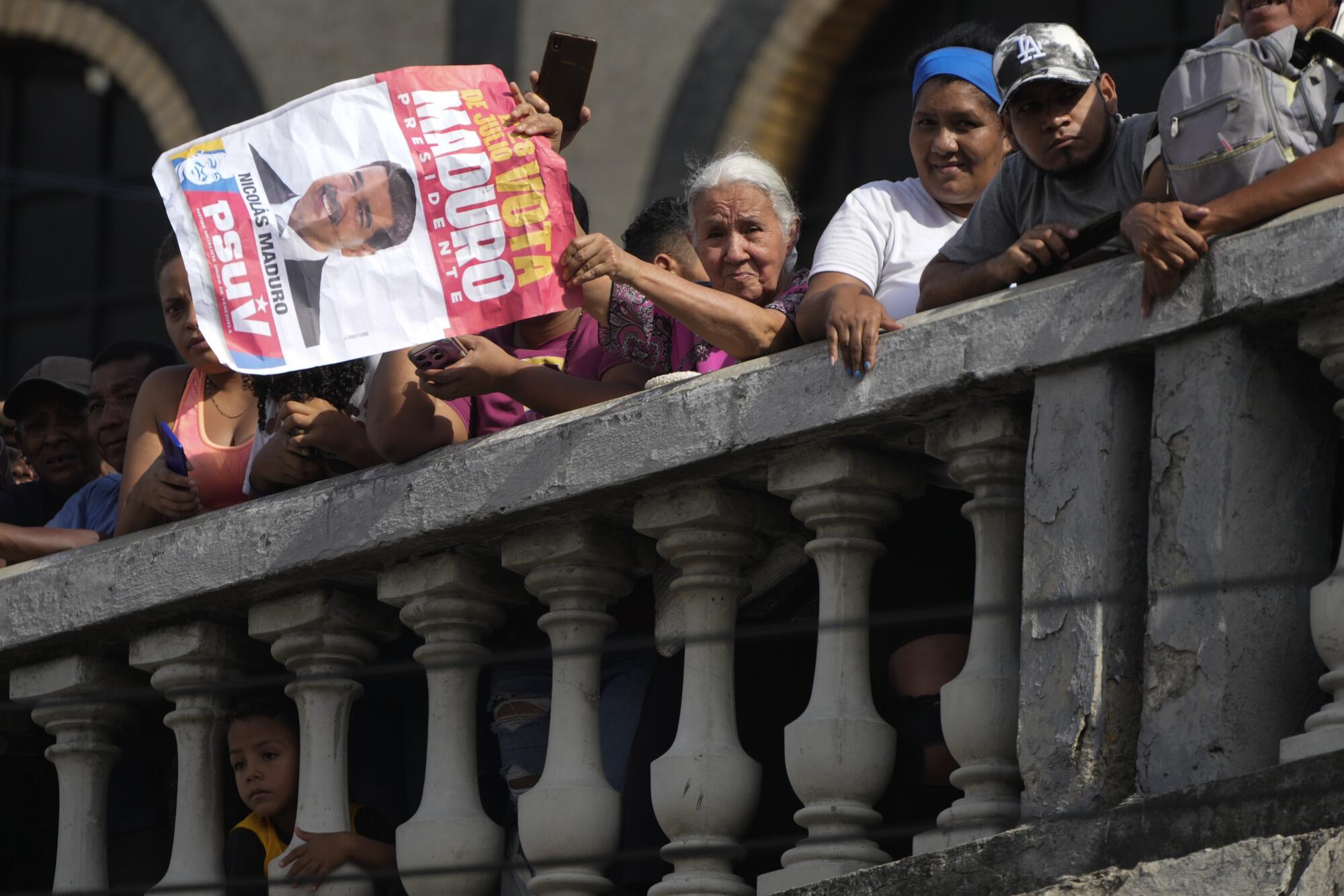 People look over a balustrade, one woman holds a Maduro campaign poster. 