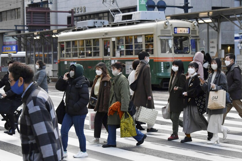 People wearing face masks cross a street in Hiroshima, western Japan Thursday, Jan. 6, 2022. Japan approved new restrictions on Friday to curb a sharp rise in coronavirus cases in the three most affected southwestern regions of Okinawa, Yamaguchi and Hiroshima. (Kyodo News via AP)