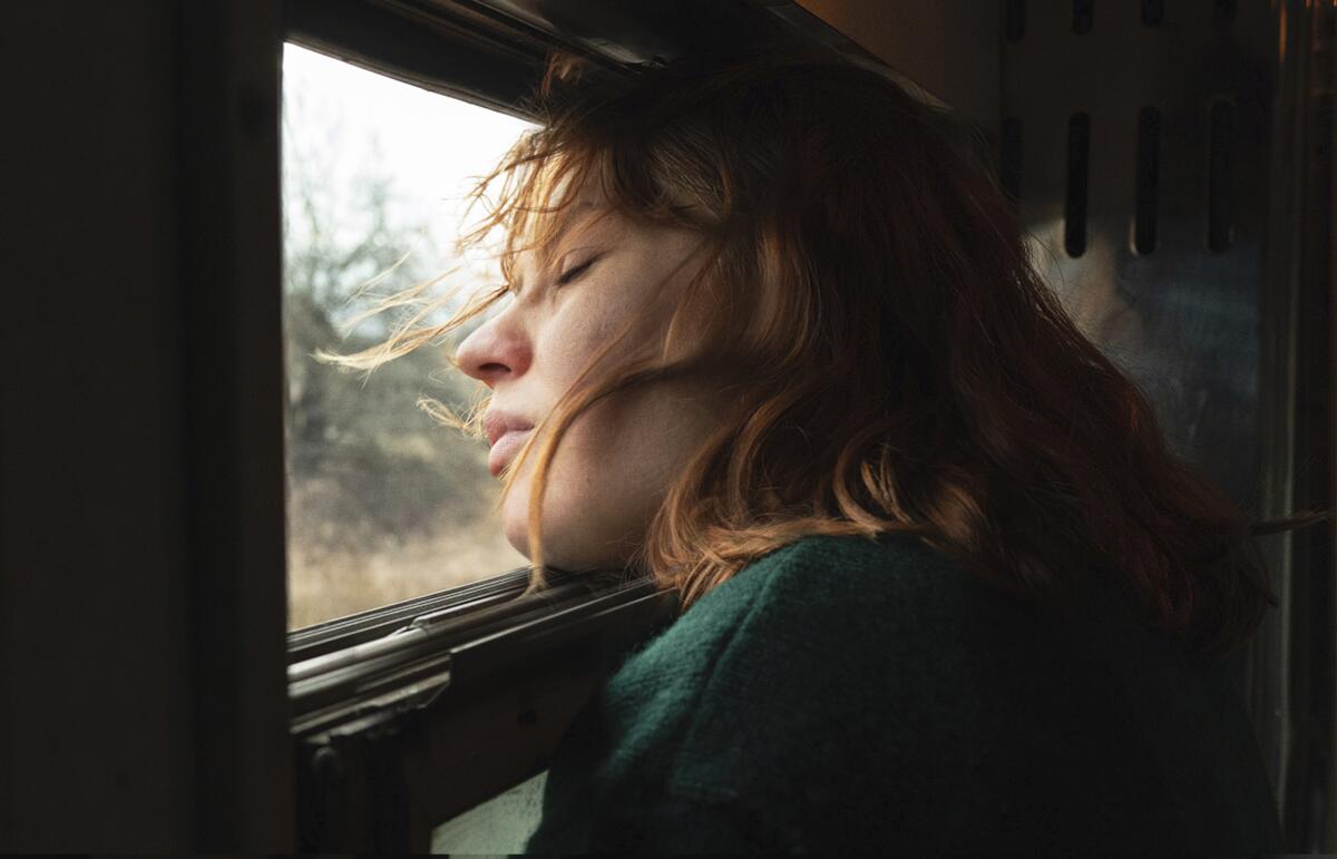 A young woman with her eyes closed leans her head against the window in a train.