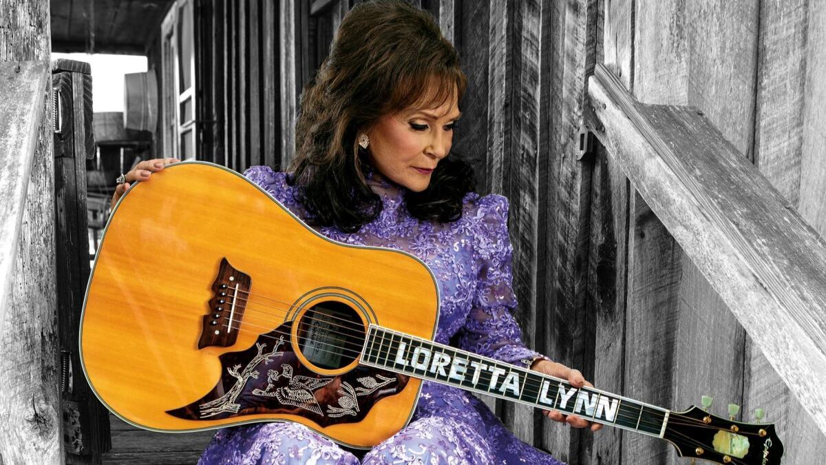 Loretta Lynn sits on a set of stairs holding a guitar with her name inlaid on the neck