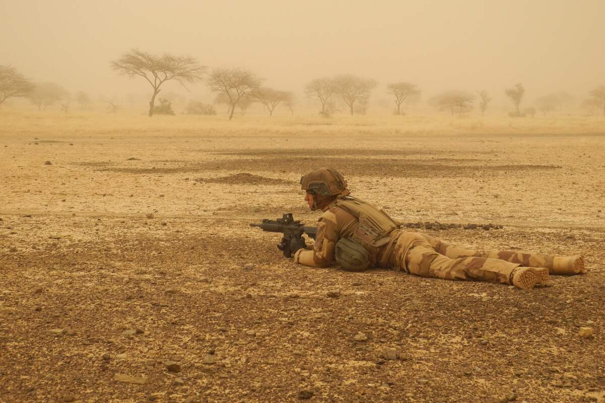 A soldier lies on the ground aiming his weapon