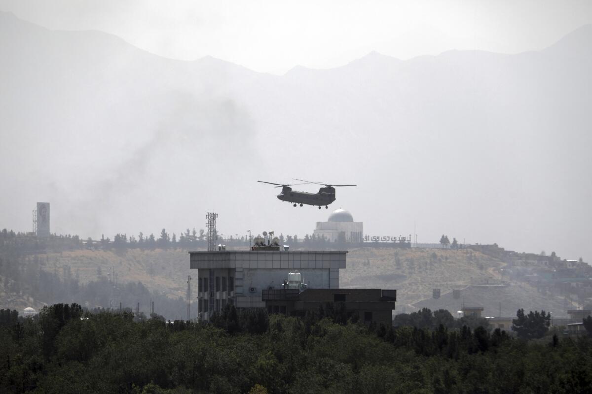 A helicopter hovers over a building against the backdrop of a mosque and mountains